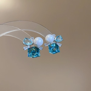 Macro shot of silver stud earrings with sea blue crystal, pearl, and zircon stones