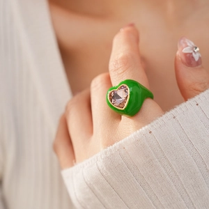 Close-up of a green heart-shaped ring with a pink stone inlay on a gold-plated band