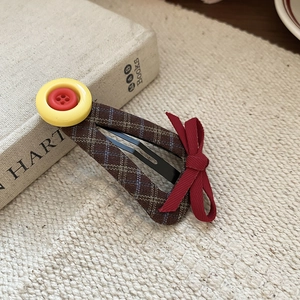 Close-up of brown plaid hair clip with yellow button and small red ribbon detail