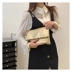 Detalle del bolso de mano metálico oro champán con diseño plegable y cremallera dorada