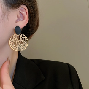 Nahaufnahme von hohlen geometrischen Goldohrringen mit schwarzem ovalem Stecker-Detail