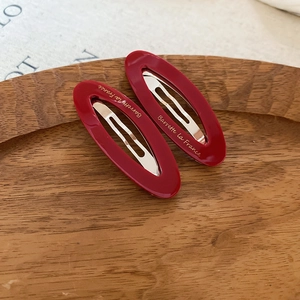 Pair of oval burgundy hair clips with gold lettering on a wooden display tray