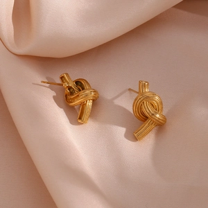 Detailed close-up of golden knotted stud earrings on a pink silk fabric background