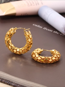 Close-up of golden U-shaped stainless steel earrings with textured scale-like pattern