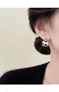 Close-up of gold-plated rocking horse earring with pearl stud and sparkling zircons