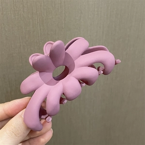 Vista detallada de una pinza para el cabello con flor rosa mate sostenida en la mano