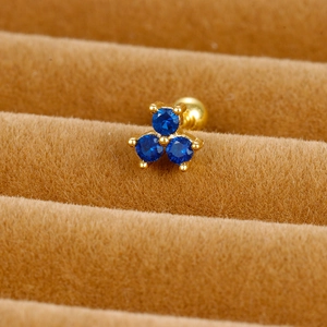 Macro shot of three royal blue zircons in a gold clover ear stud on brown velvet