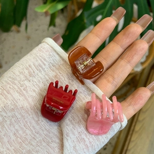 Close-up of small acetate hair claws in brown, red and pink with gold handmade label