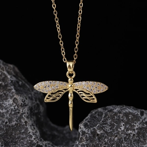 Close-up of golden dragonfly pendant necklace with crystal wings on dark rock base