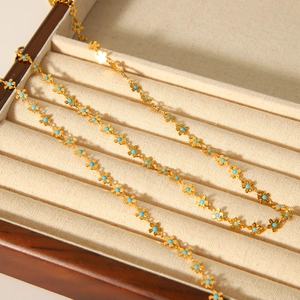 Close-up of golden stainless steel necklaces with blue flower charms in a wooden jewelry box