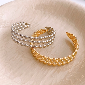 Close-up of gold and silver triple-row beaded open bangles on a ceramic tray