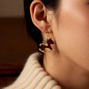 Detail of elegant gold horse earrings with red enamel and zircon accents on a model