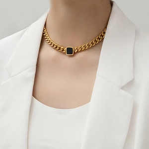 Gold thick chain necklace with black square pendant worn on a minimalist blazer