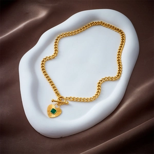 Golden cuban chain necklace with green heart pendant and OT clasp on a white plate