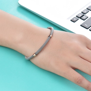 Detail of grey stainless steel mesh bracelet with rose gold rings on a teal desk surface