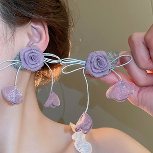Detail of purple fabric rose earrings with long tassels on a model for a resort look