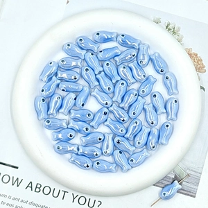 Macro shot of light blue ceramic fish beads with iridescent glaze in a white plate