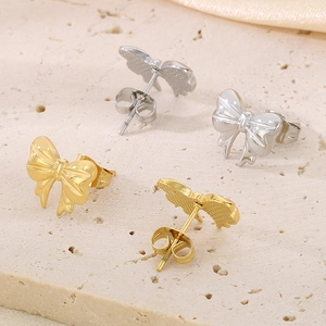 Gros plan de boucles d'oreilles nœud papillon en acier doré et argenté avec détails d'ailes