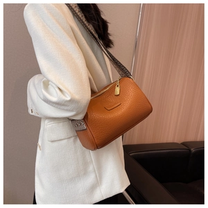 Detail der orangefarbenen Crossbody-Tasche mit gewebtem Riemen und goldener Hardware