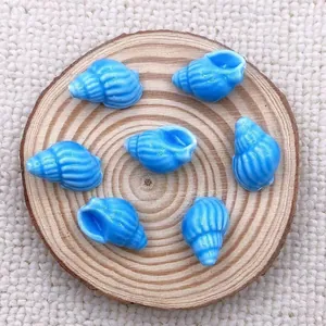 Detailed view of seven blue conch-shaped ceramic beads on a wooden tray for DIY jewelry