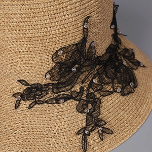 Detailed close-up of woven straw texture with black lace floral patch and beads