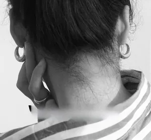Artistic close-up of model wearing chunky metal hoop earrings and minimal smooth rings