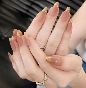 Macro detail of long almond press-on nails with nude base and gold French metallic tips