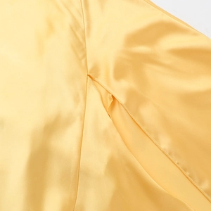 Detailed close-up of glossy bright yellow satin fabric texture and premium stitching