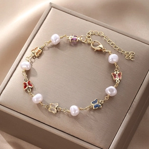Detail of gold butterfly bracelet with colorful charms and white pearls on satin