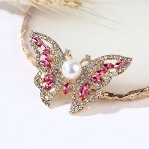 Elegant gold butterfly brooch with pearls and pink rhinestones on white jewelry plate