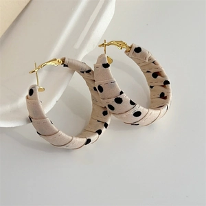 Detail of C-shaped beige fabric-wrapped hoop earrings with black polka dot pattern