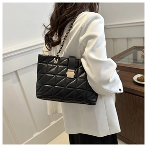 Classic black quilted tote bag with chain strap shown on a model in a white blazer
