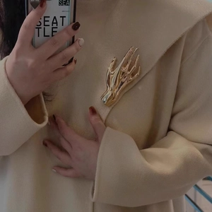 Detailed close-up of a golden hand-shaped brooch on a beige textured wool coat lapel