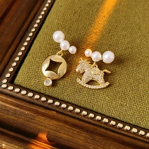 Détail de boucles d'oreilles asymétriques dorées avec cheval et pièce sur velours vert