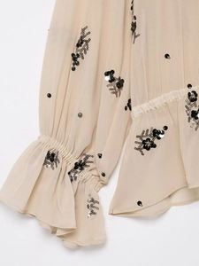 Detail of beige chiffon blouse featuring black sequin floral embroidery and ruffle cuffs