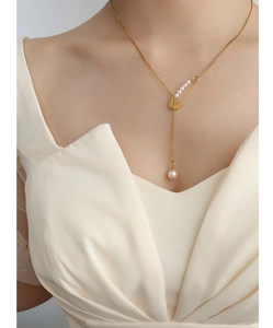 Detailed shot of the gold safety pin pendant with white pearls on a layered chain