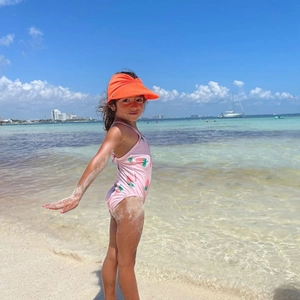 Girl's strawberry print swimsuit and orange sun hat on a sunny beach setting