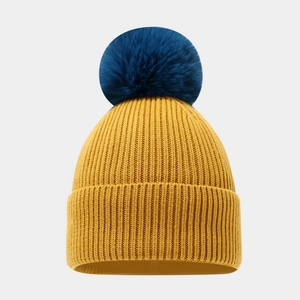 Detailed texture of mustard yellow ribbed knit beanie with a navy blue faux fur pom-pom