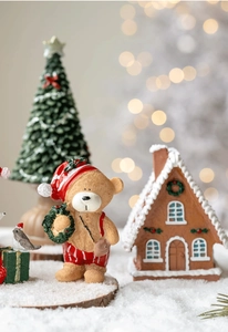 Miniature resin Christmas scene with teddy bear, snowy house and tree on a festive background