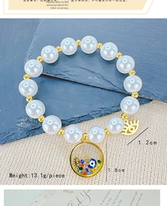 Detail of beaded pearl bracelet with gold evil eye and hamsa hand charms on blue stone