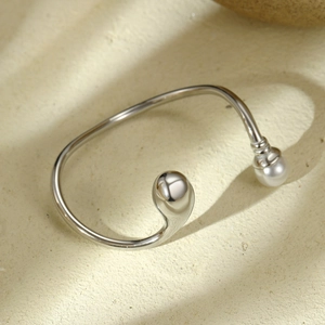 Détail d'un bracelet argenté en forme de goutte avec perle blanche sur texture naturelle
