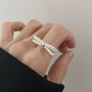 Detail of a double-layer crossover pearl ring on finger with silver-tone accents