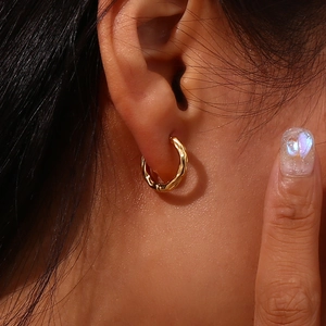 Close-up of golden lava textured small hoop earring worn on an earlobe