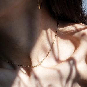 Artistic close-up of gold pear and square zircon necklace on model with light shadows