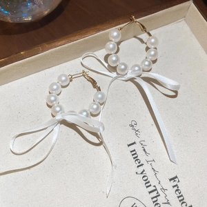 Detail view of elegant French style pearl hoop earrings decorated with white ribbon bows.