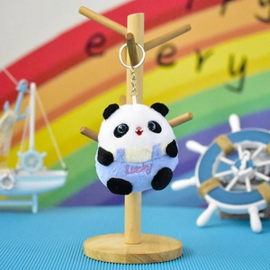 Detailed view of a cute plush panda keychain wearing blue Lucky overalls on a stand