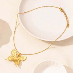 Close-up of golden stainless steel necklace featuring a hollow butterfly pendant on ceramic