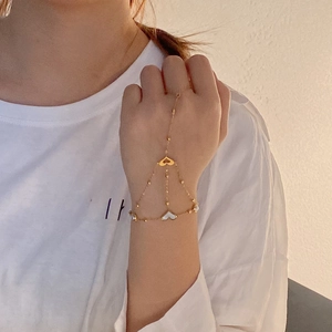 Detail of gold finger bracelet featuring heart charms and pearl accents on model's hand