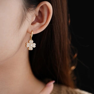 Macro shot of a model wearing a gold clover earring with pearls and zircon crystals