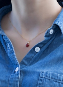 Detail of red round gemstone necklace with gold chain worn on female model